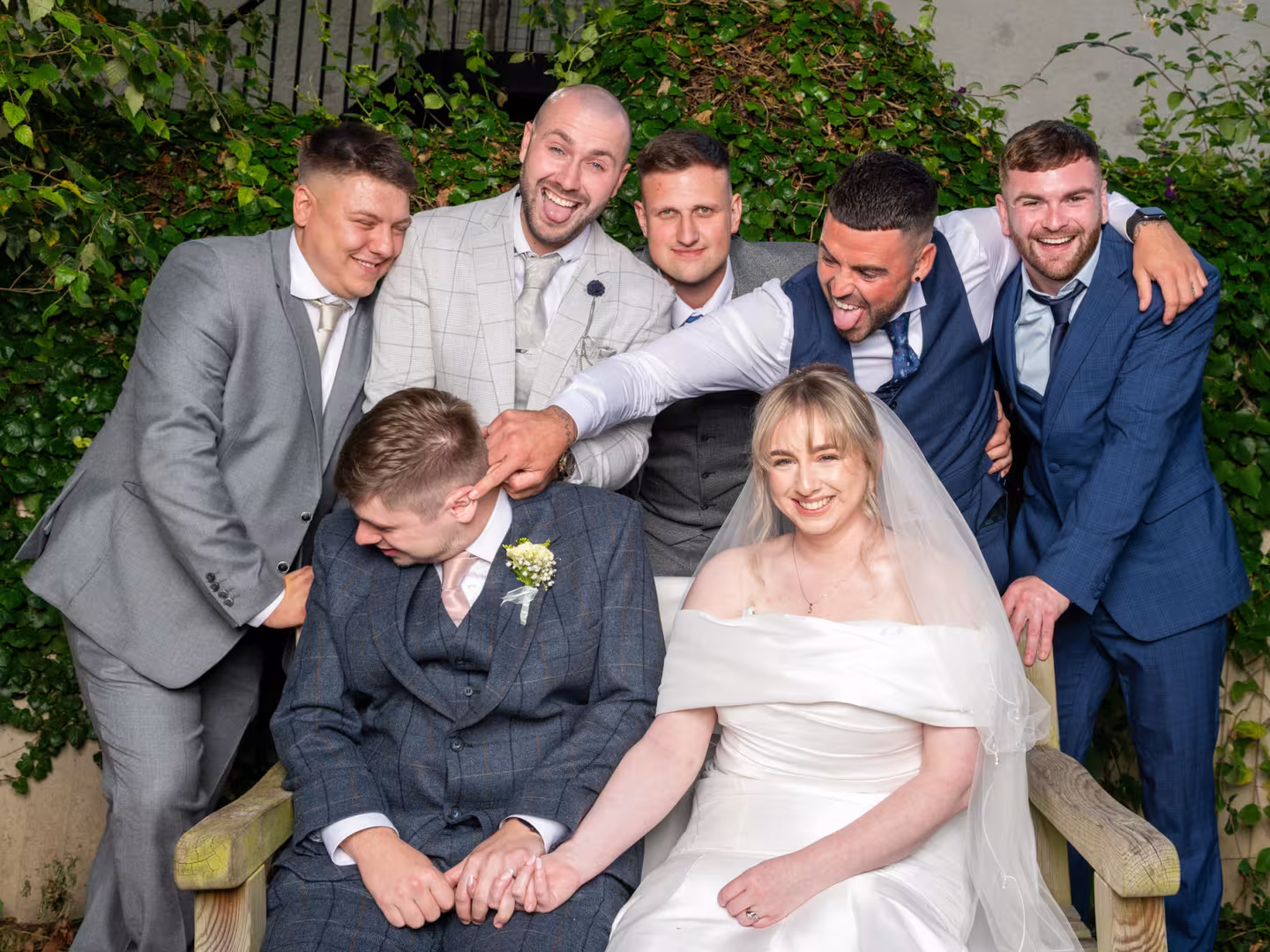 Bride and groom sitting on a bench while the grooms men pester the groom