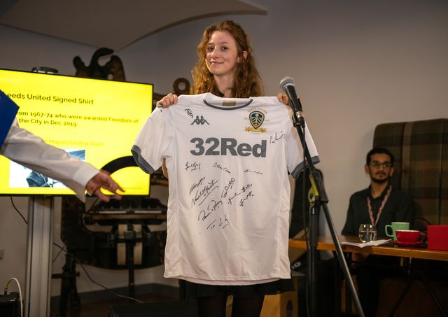 A woman hold a signed leeds shirt for auction