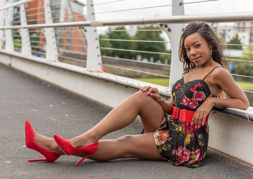Woman in black and red dress with red shoes sitting on a bridge