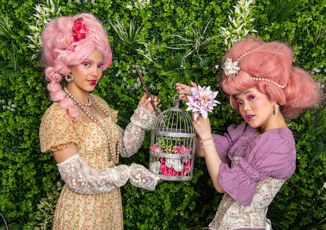 Two ladies with big pink wigs holding a bird cage
