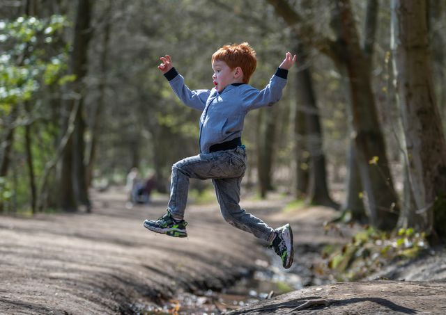 Young boy jumping across a stream in a forest