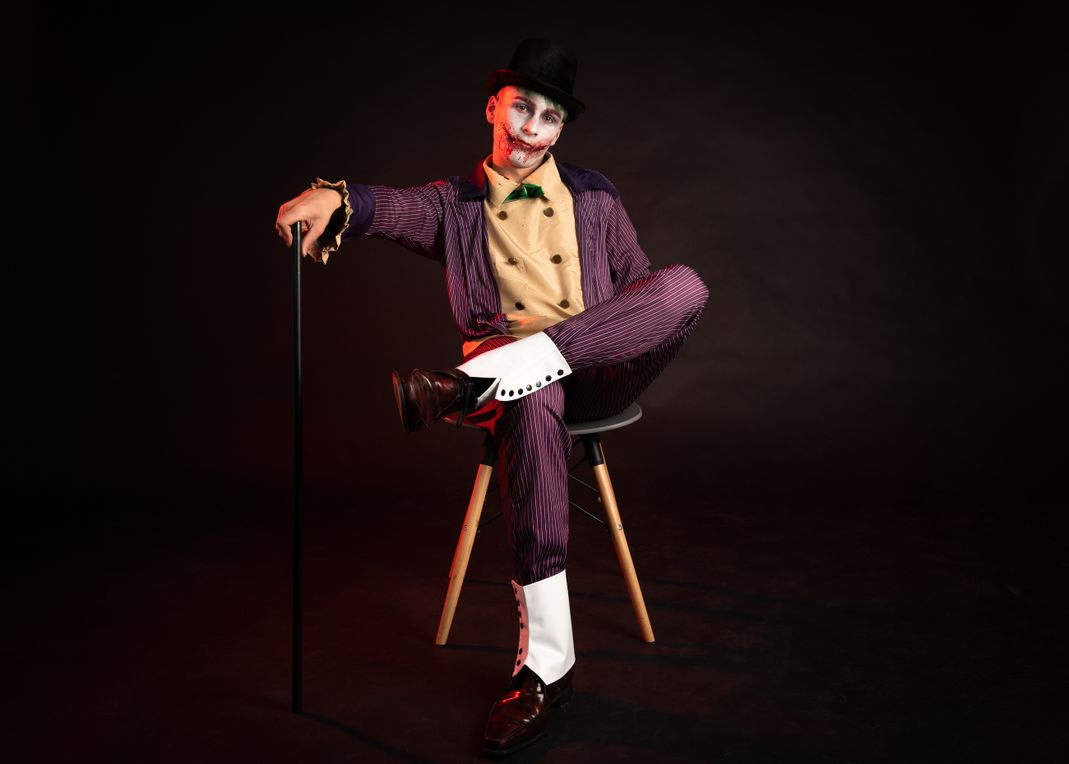 The joker sitting on a chair with a cain 