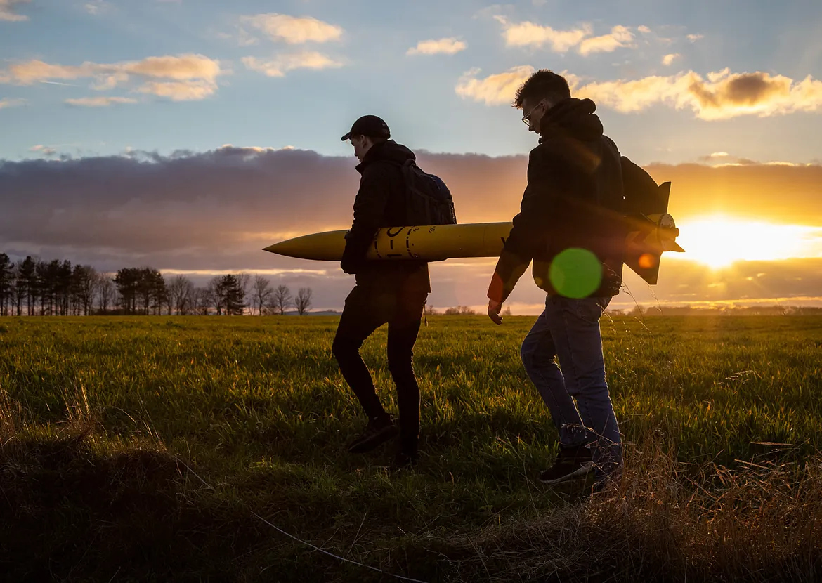 Two students walking a rocket to the launch sight at sun set