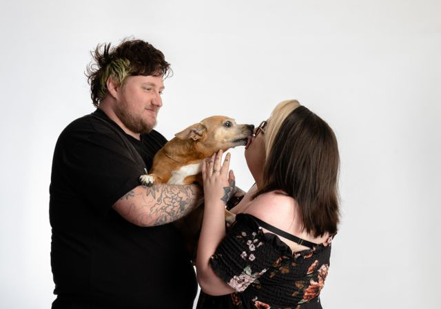 Man and woman hold dog between them and dog kissing woman