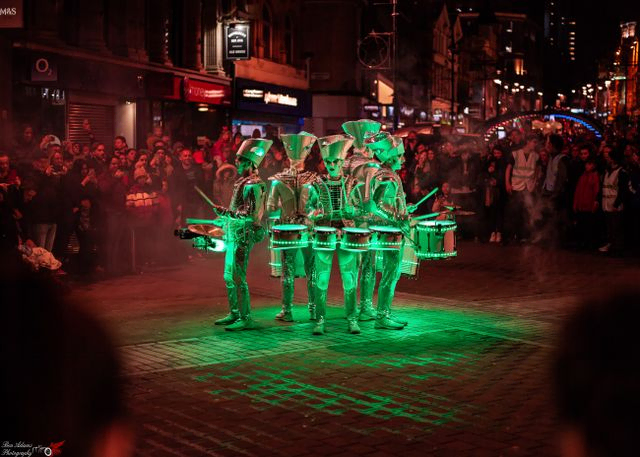 five drummers in a crown covered in green lights