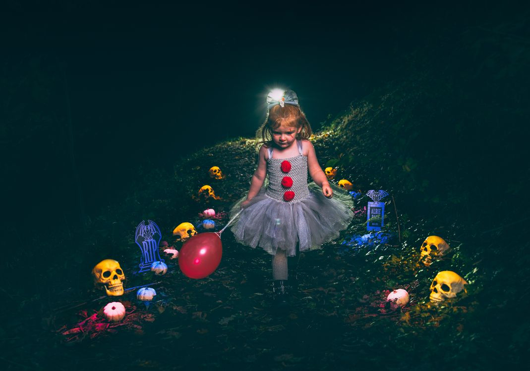 Little girl dress as IT walking down a path of skulls