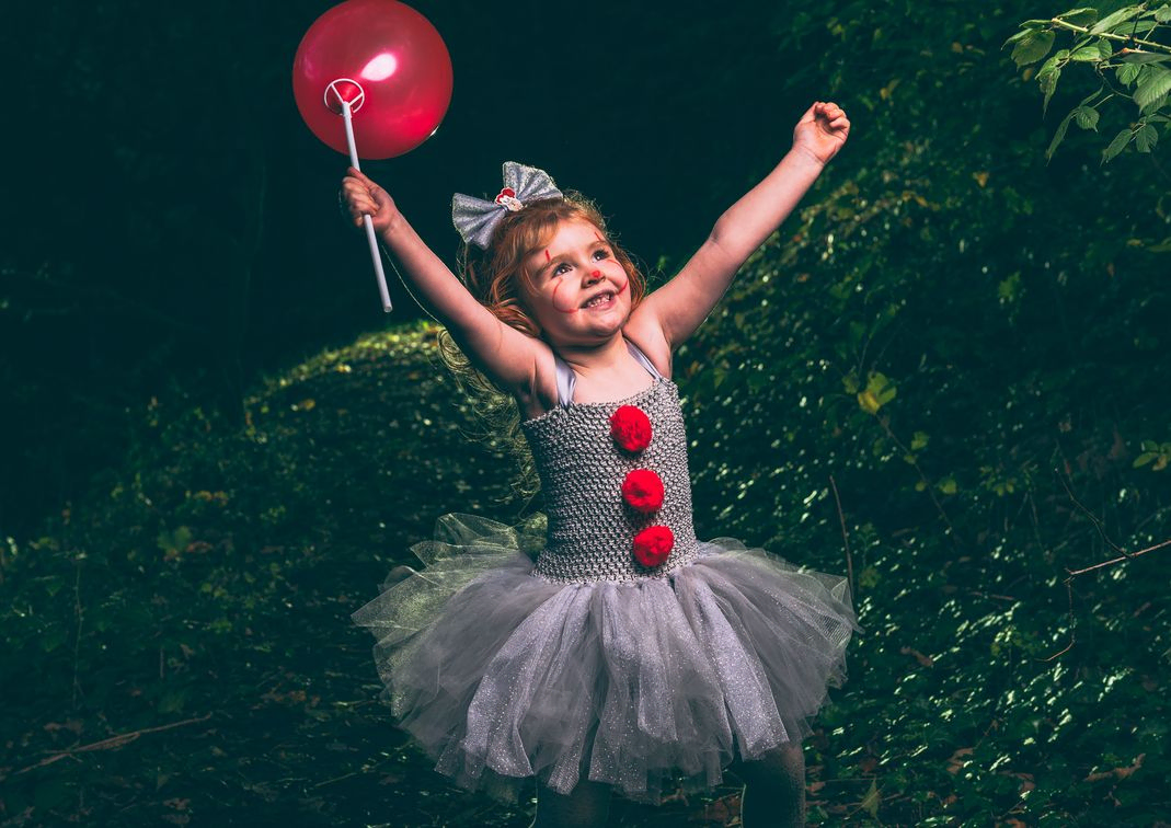 Young girl dress as IT holding a balloon with arms in the air