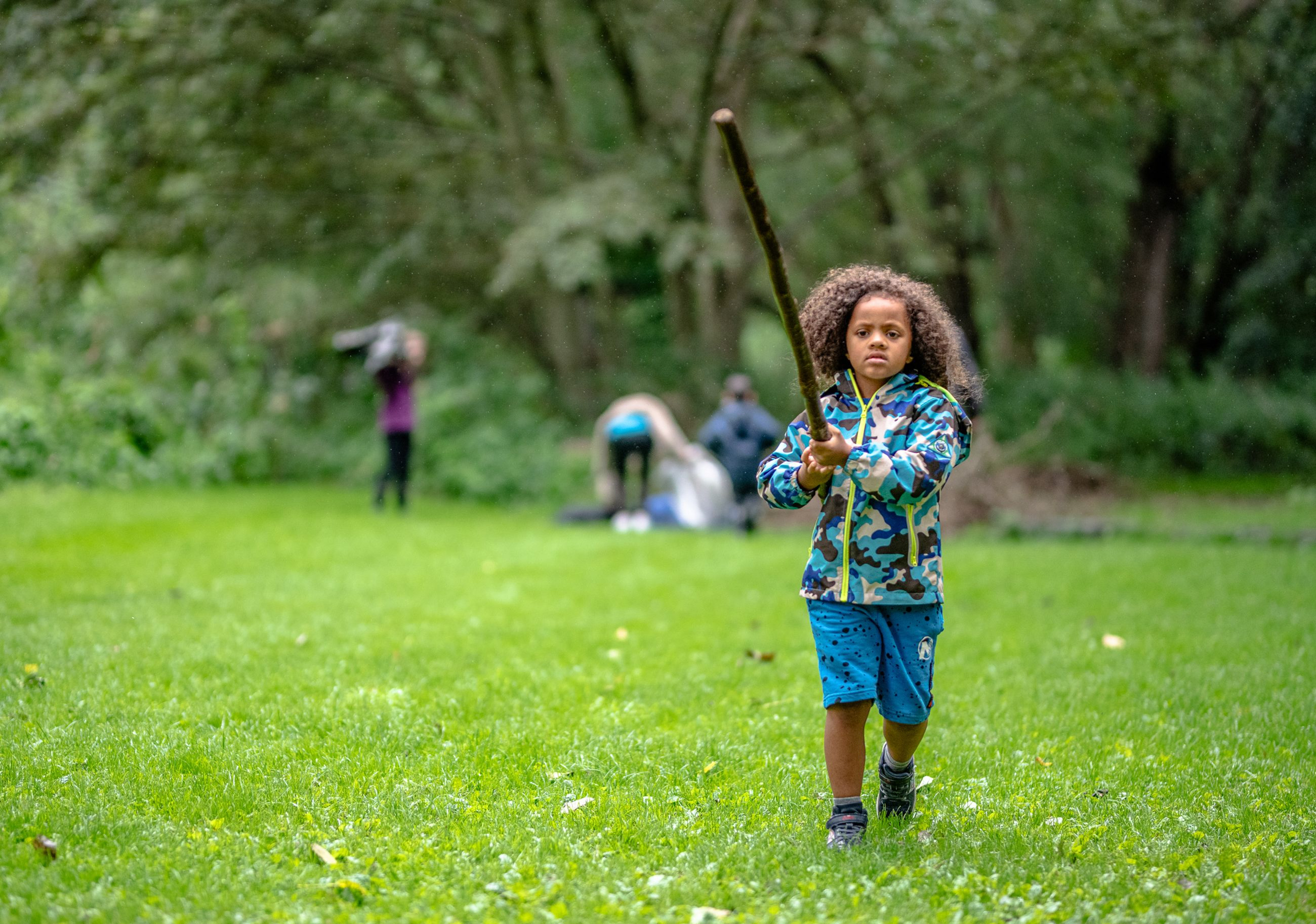 Child carrying a large stick across a field