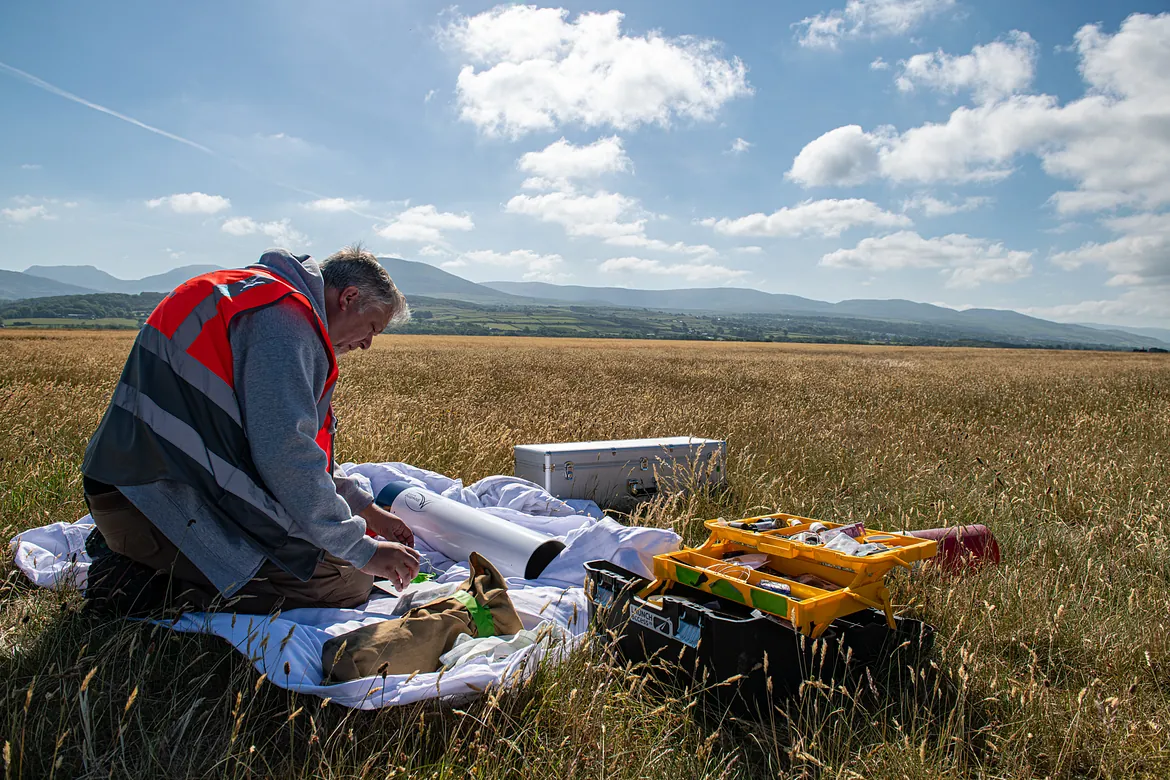 A man sitting on the ground in a field building a rocket