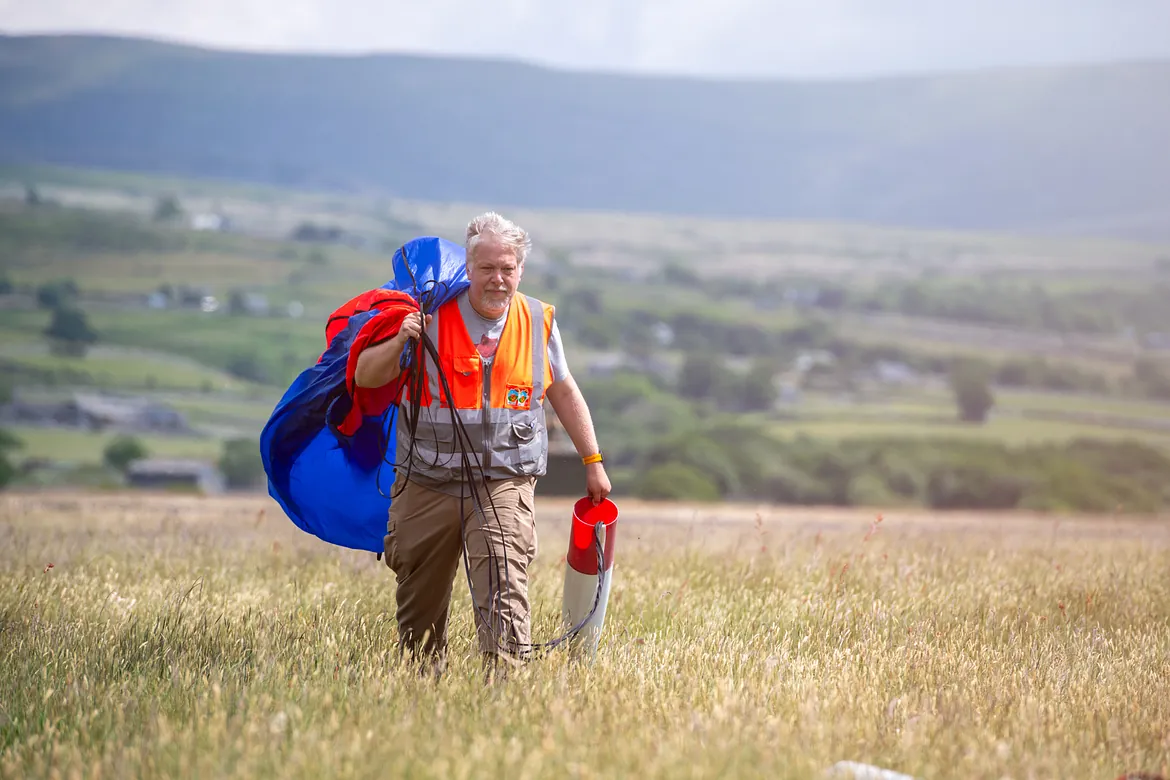 A man in high vis vest walking with rocket and deployed parachute 